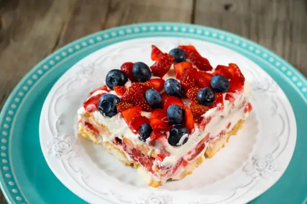 Tranche de tiramisu aux fruits rouges, garnie de fraises et myrtilles fraîches, sur une assiette blanche ornée.
